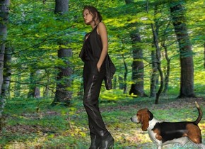 a flat wall.a woman is in front of the wall.the ground is clear.the wall is [forest].the wall is 2 inches in the ground.the woman is facing southwest.it is evening.a dog is right of the woman.the dog is facing the woman.